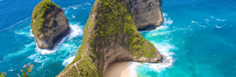 Steep cliffs with lush greenery surround a small sandy beach and turquoise ocean waves.
