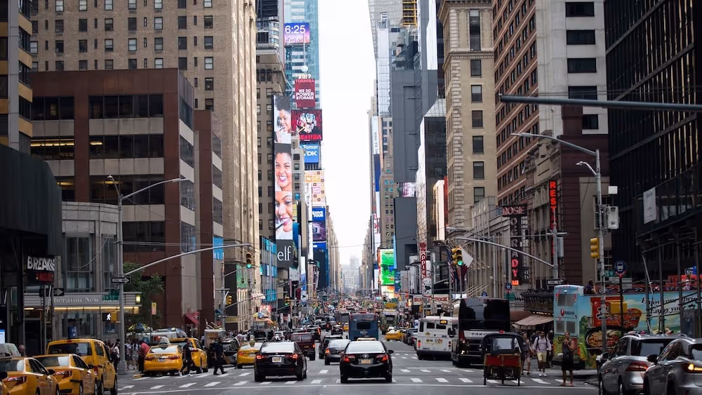 Busy city street with tall buildings, yellow taxis, cars, and people walking in New York City’s Times Square.