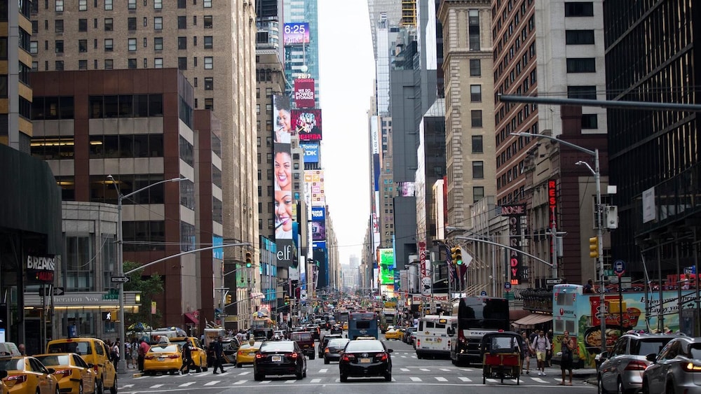 Busy city street with tall buildings, yellow taxis, cars, and people walking in New York City’s Times Square.