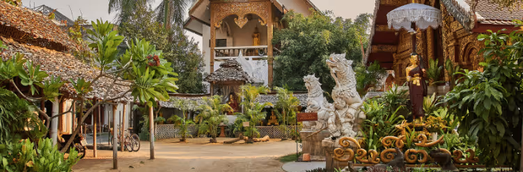 Ornate temple courtyard with dragon statues, lush greenery, and intricate wooden architecture in sunlight.