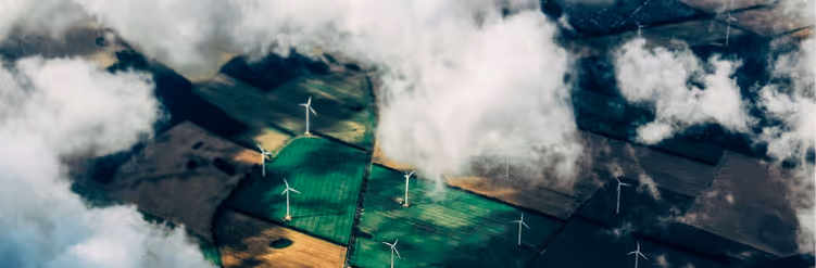 Aerial view of wind turbines scattered across green and brown fields, partially covered by clouds.