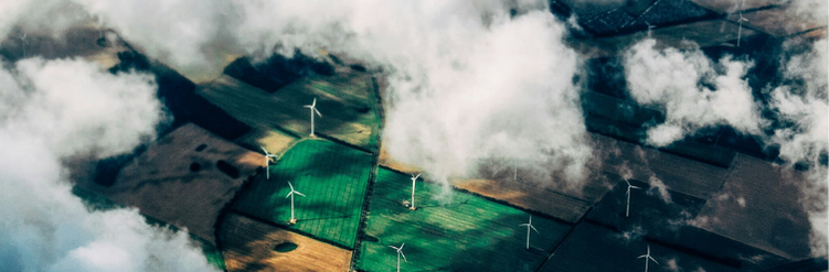 Aerial view of wind turbines scattered across green and brown fields, partially covered by clouds.
