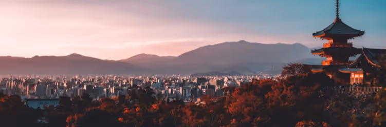 A cityscape with a traditional Japanese pagoda in the foreground and mountains in the background during sunset, illustrating a serene blend of cultural heritage and sustainable business travel opportunities amidst stunning natural scenery. | Dyme