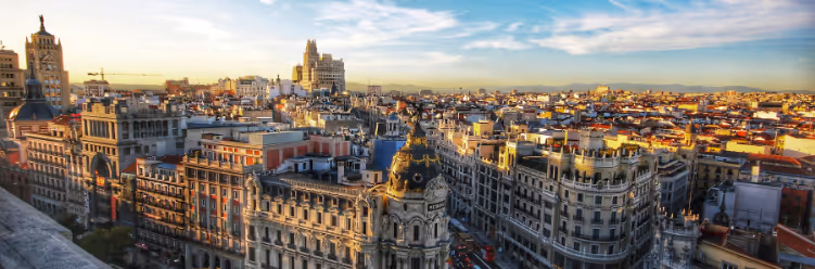 Panoramic view of a city with historic architecture, including ornate buildings and domes, under a clear blue sky at sunset—a perfect blend of tradition with modernity for sustainable business travel. | Dyme
