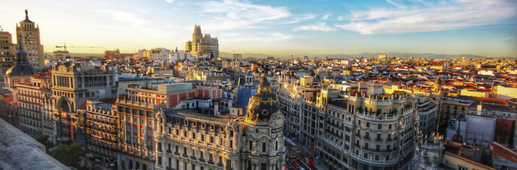 Panoramic view of a city with historic architecture, including ornate buildings and domes, under a clear blue sky at sunset—a perfect blend of tradition with modernity for sustainable business travel. | Dyme
