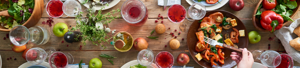 A table set with salads, fruit, bread, wine, and a plate of roasted vegetables being served.