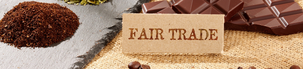 A Fair Trade sign next to chocolate, coffee grounds, and coffee beans on a burlap surface.
