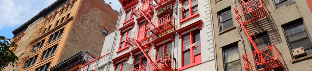 City buildings with red fire escapes on the facades, photographed from a street-level angle.