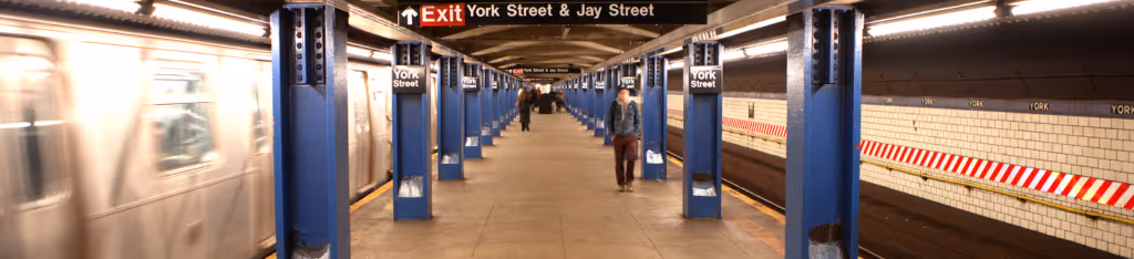 A person walks on the York Street subway platform as a train approaches on the left in a blurred motion.