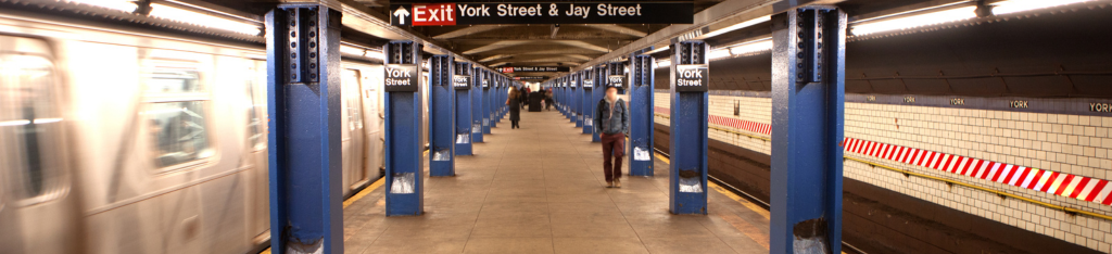 A person walks on the York Street subway platform as a train approaches on the left in a blurred motion.