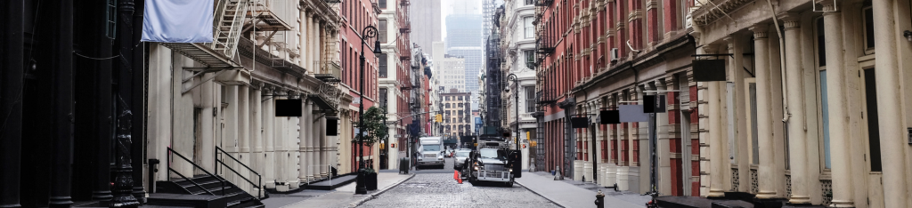A cobblestone street lined with historic buildings and parked cars in an urban cityscape.