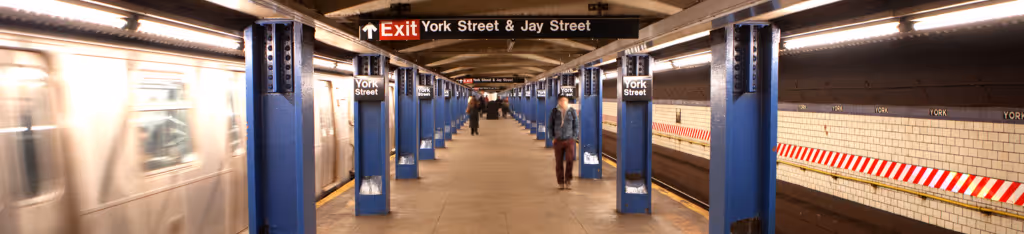Blurred subway train departing York Street station, blue columns, tiled walls, and people on the platform.