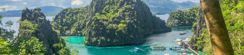 Scenic view of limestone cliffs, turquoise water, and boats docked in a tropical bay surrounded by lush greenery.