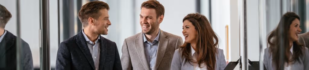 Three business professionals smiling and talking together in an office hallway.