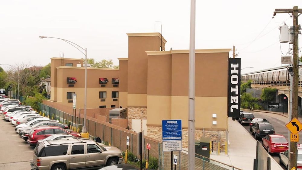 A tan and brown hotel with a black vertical HOTEL sign, next to a parking lot filled with cars.
