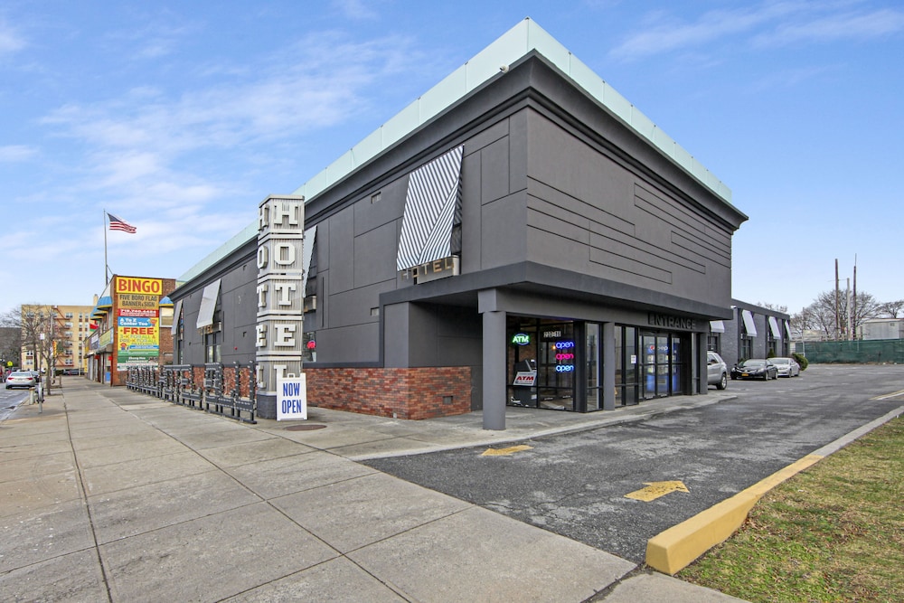 Modern gray hotel building with large HOTEL sign, parking lot, and sidewalk under a clear blue sky.