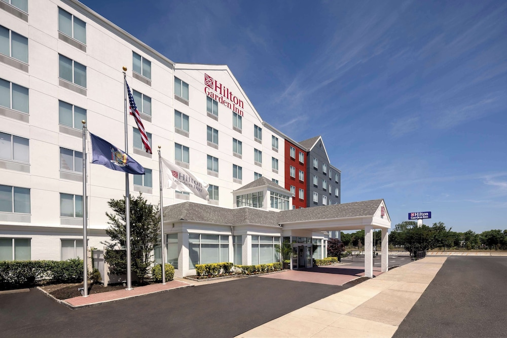 Hilton Garden Inn hotel exterior with flags, driveway, and clear blue sky.