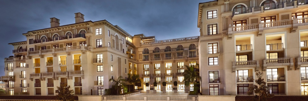 Elegant multi-story building with lit windows and balconies, photographed at dusk against a cloudy sky.