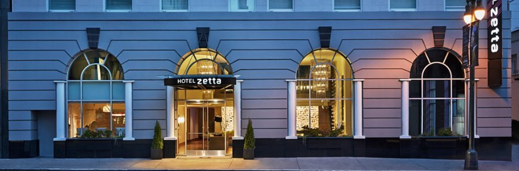 Hotel Zetta entrance with large arched windows and a lit sign at dusk on a city street.
