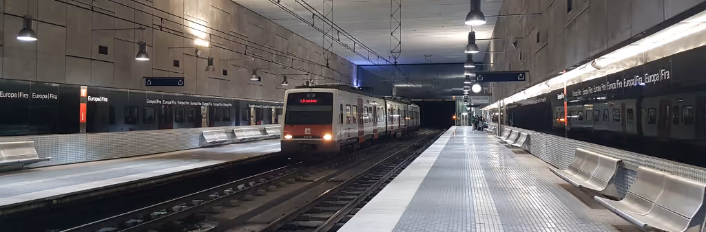 A train arrives at a modern, well-lit underground station with empty platforms and benches.