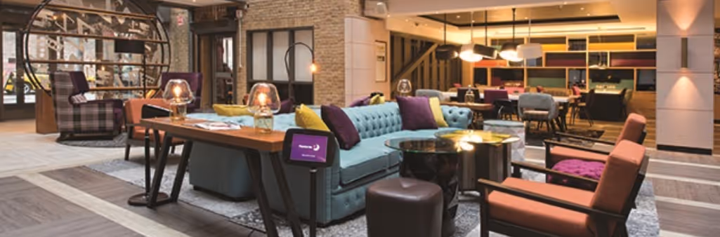 Modern hotel lobby with colorful sofas, armchairs, tables, and warm lighting in a stylish, open space.