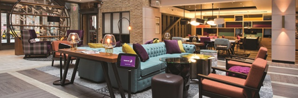 Modern hotel lobby with colorful sofas, armchairs, tables, and warm lighting in a stylish, open space.