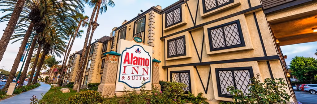 Alamo Inn & Suites sign in front of a tan hotel building with palm trees lining the sidewalk.