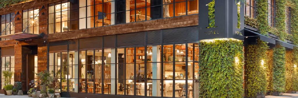 Modern hotel exterior with large windows, wooden panels, and walls covered in green plants and vines.