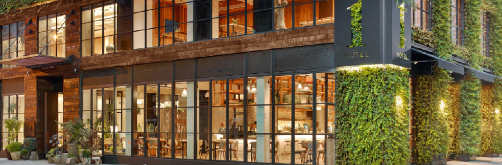 Modern hotel exterior with large windows, wooden panels, and walls covered in green plants and vines.