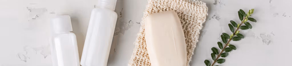 Two white bottles and a bar of soap rest on a textured mat beside a small green branch on a light gray surface, creating an ideal setting for presenting an Honest Company gift card.