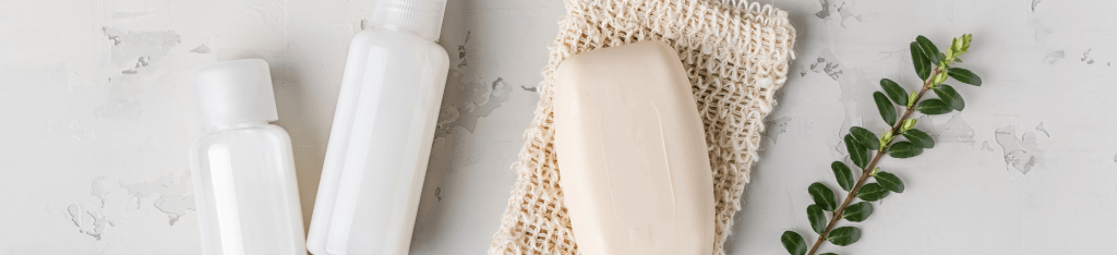 Two white bottles and a bar of soap rest on a textured mat beside a small green branch on a light gray surface, creating an ideal setting for presenting an Honest Company gift card.
