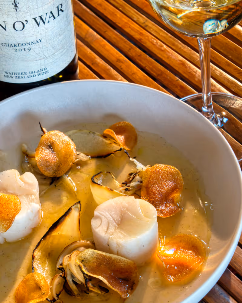 Bowl of scallops with grilled onions and crispy chips, served with a glass of white wine and a bottle of Chardonnay.
