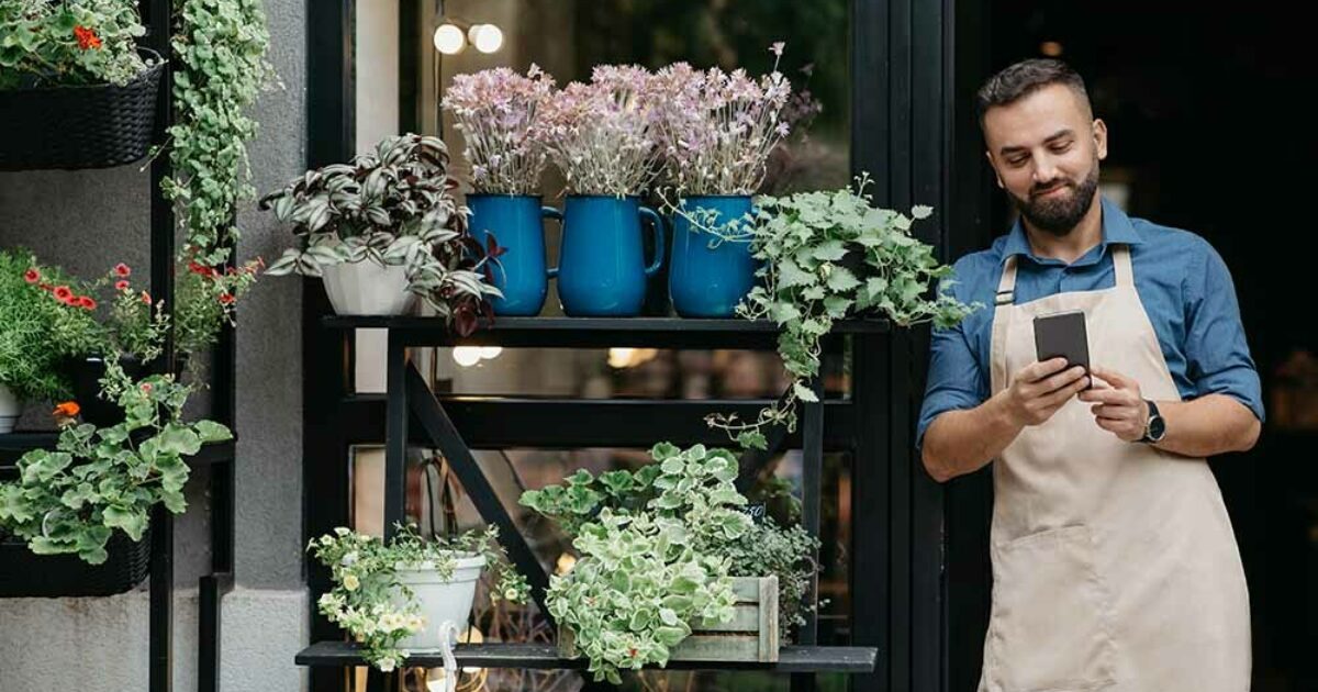 Ragazzo in piedi davanti alla porta del suo negozio guardando il tablet