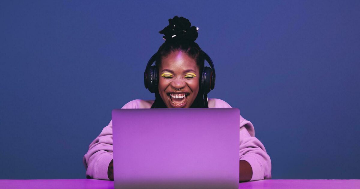 Woman smiling while looking at her laptop with headphones on
