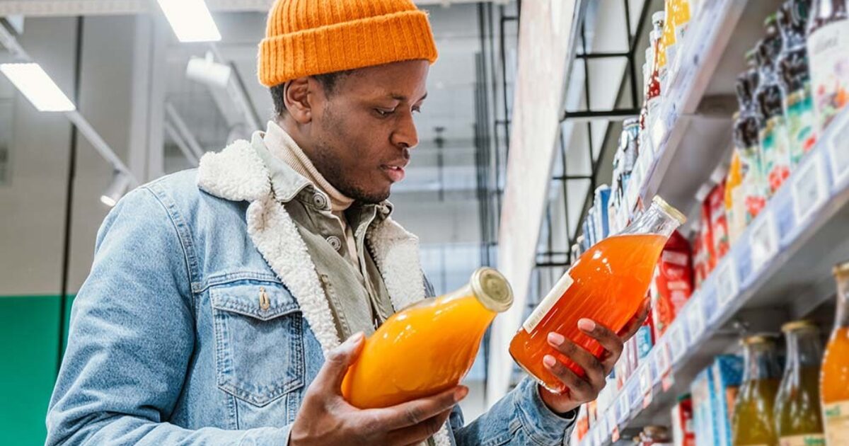 Homme comparant des bouteilles de jus dans une allée de supermarché