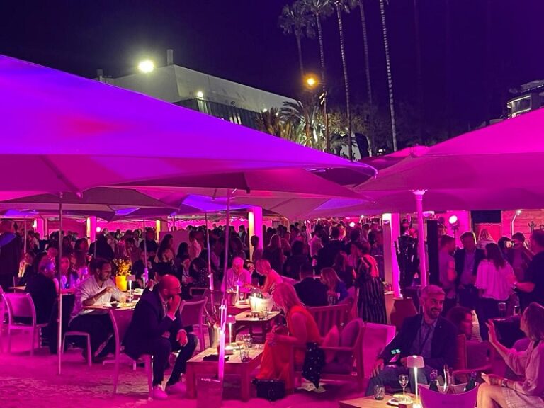 Soirée en bord de plage avec éclairage rose, palmiers et invités à Cannes