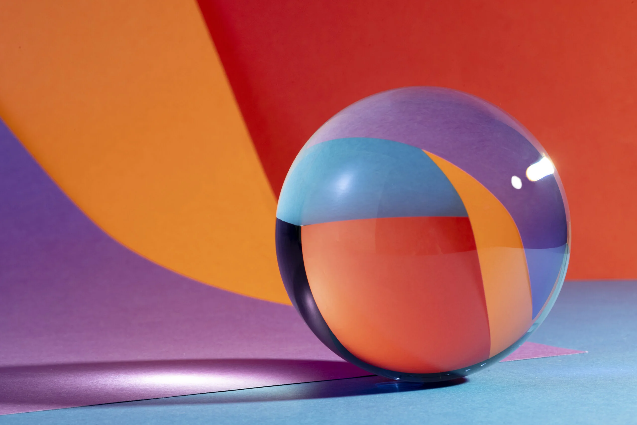 Clear glass sphere on colorful geometric background with bold orange, red, purple, and blue sections.