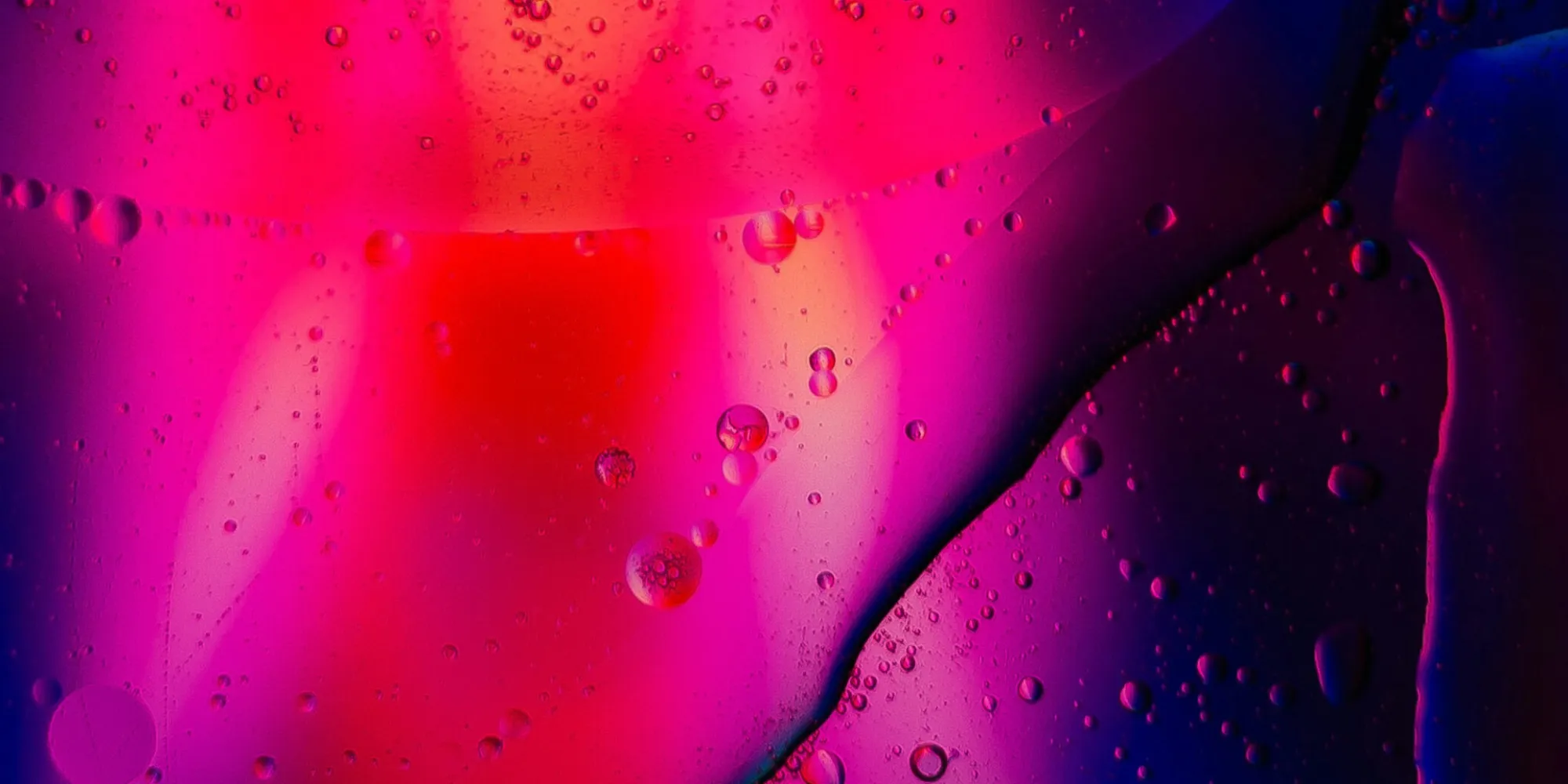 A macro photograph of abstract fluids, likely oil and water, creating a pink & purple texture.