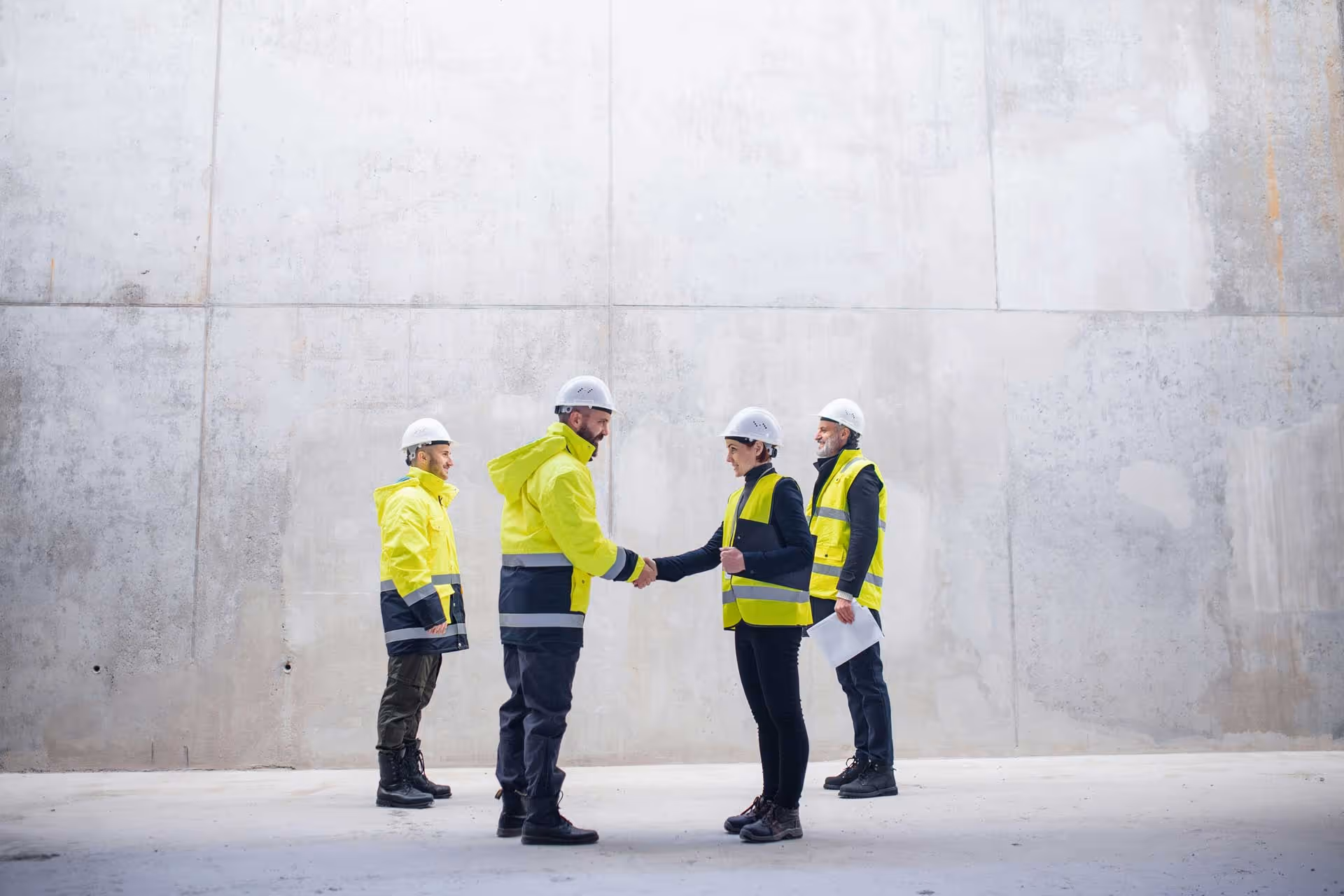 A group of construction workers meeting in a concrete building with hard hats and PPE on.