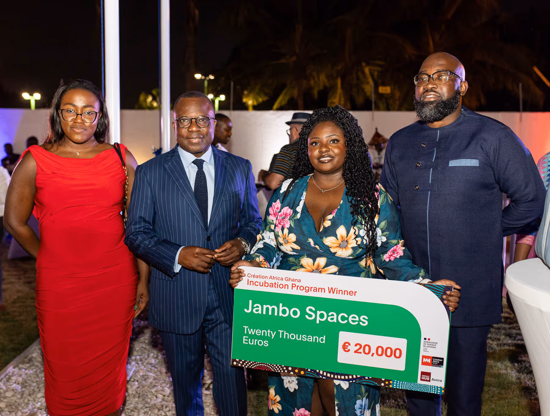Four people standing outdoors at night, one woman holding a large check for €20,000 awarded to Jambo Spaces as Creation Africa Ghana Incubation Program Winner.