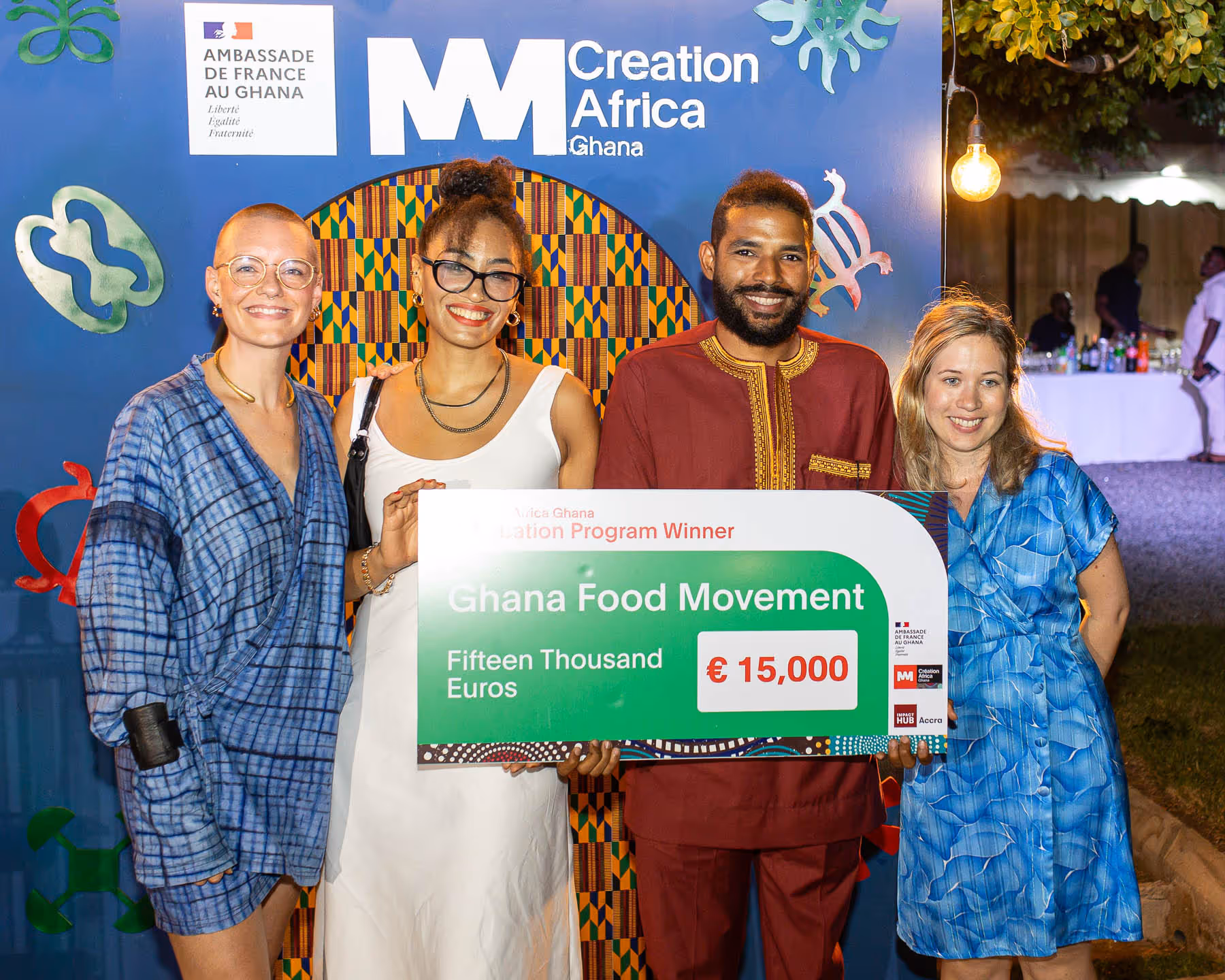 Four people smiling and holding a large check for €15,000 awarded to Ghana Food Movement at a Creation Africa Ghana event.