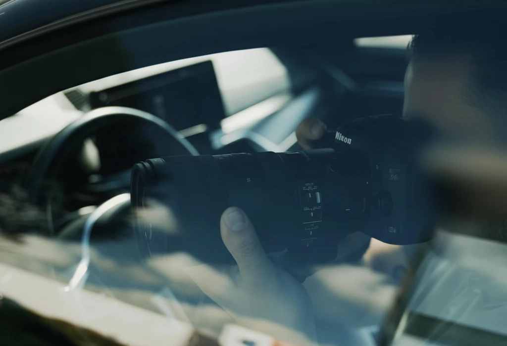 Personne tenant un appareil photo Nikon à longue focale, photographiant à travers la fenêtre d'une voiture.