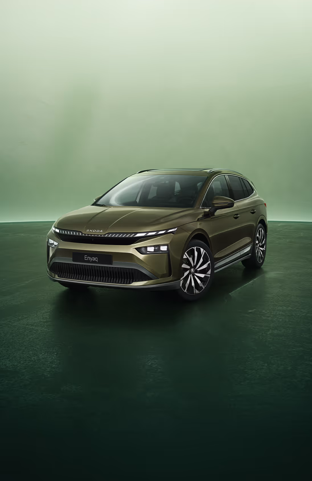Dreiviertel-Frontansicht auf einen Škoda Enyaq in der Farbe Olibo-Grün Metallic vor einem grünen Studiohintergrund. Oben links steht geschrieben "Škoda 130 Jahre". Unten rechts ist der Schriftzug "Enyaq" platziert.