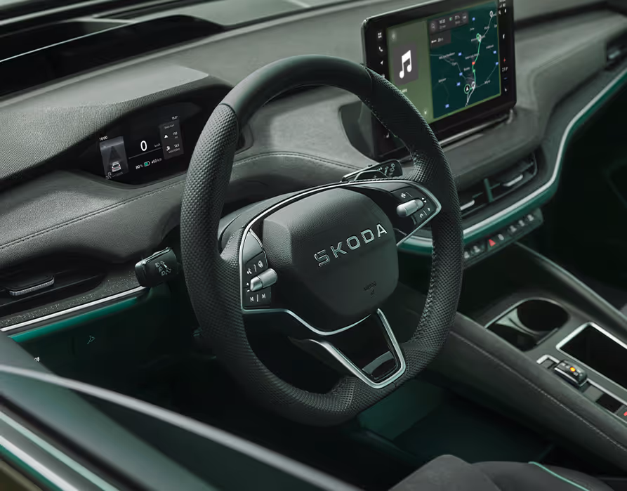 Eine Nahaufnahme zeigt das Zweispeichen-Multifunktionslenkrad im Cockpit des Škoda Enyaq. Das Lenkrad mit dem Škoda Schriftzug ist mit Multifunktionstasten und Rändelrädchen aus Chrom ausgestattet. Im Hintergrund sind das Digital Cockpit und das freistehende Infotainmentdisplay zu sehen.