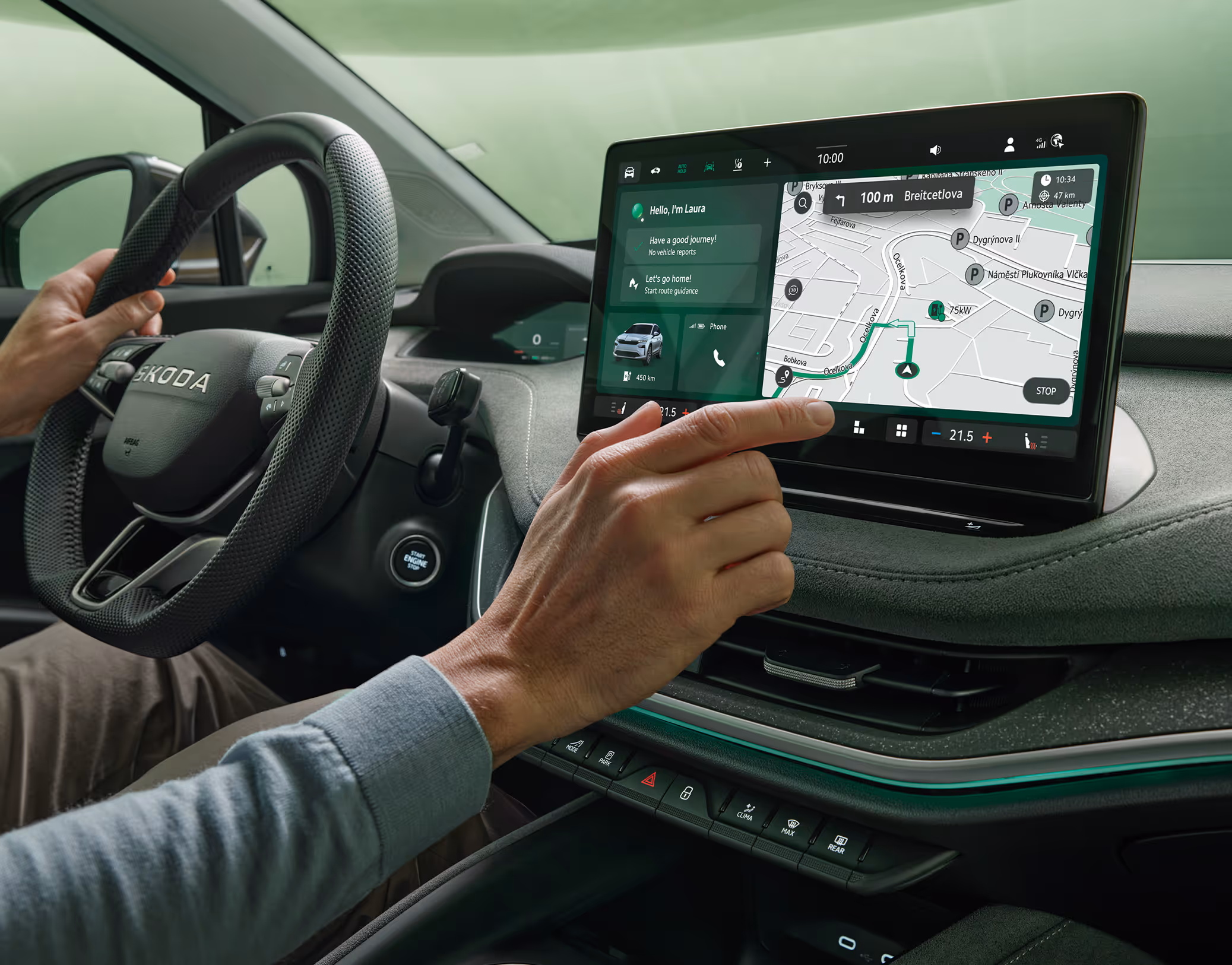Im Innenraum eines Škoda Enyaq bedient eine Person mit dem Finger das freistehende 13-Zoll-Infotainmentdisplay. Auf dem Bildschirm ist eine Navigationskarte mit einer markierten Route zu sehen, während die andere Hand am Lenkrad liegt. Das moderne Cockpit wird durch eine grüne Ambientebeleuchtung akzentuiert.