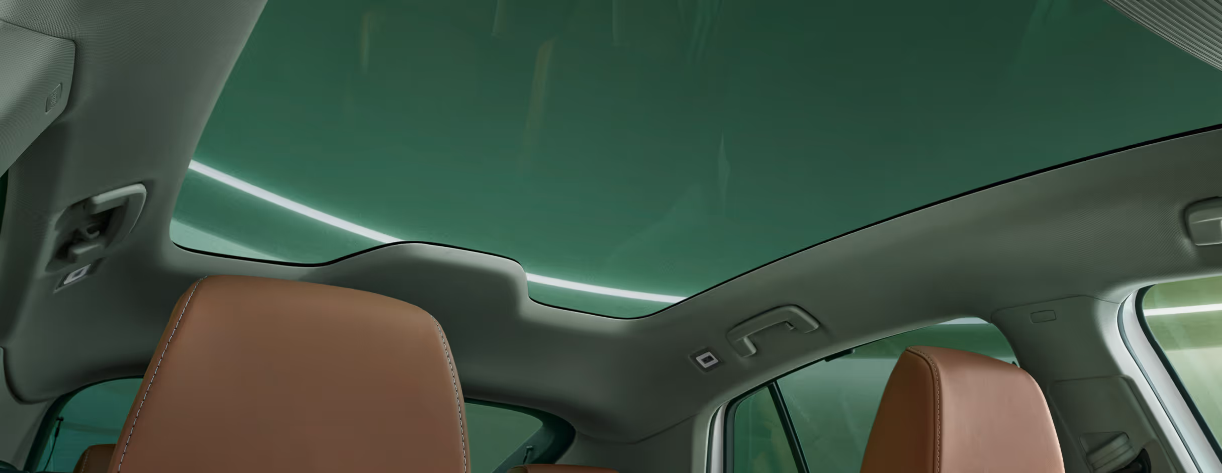 Blick von der Beifahrerseite nach oben auf das große Panoramaschiebedach des Škoda Enyaq, das sich über den gesamten Innenraum erstreckt. Das getönte Glasdach flutet den Innenraum mit Licht und vermittelt ein großzügiges Raumgefühl, was die cognacbraunen Ledersitze der Design Selection „ecoSuite“ zur Geltung bringt.