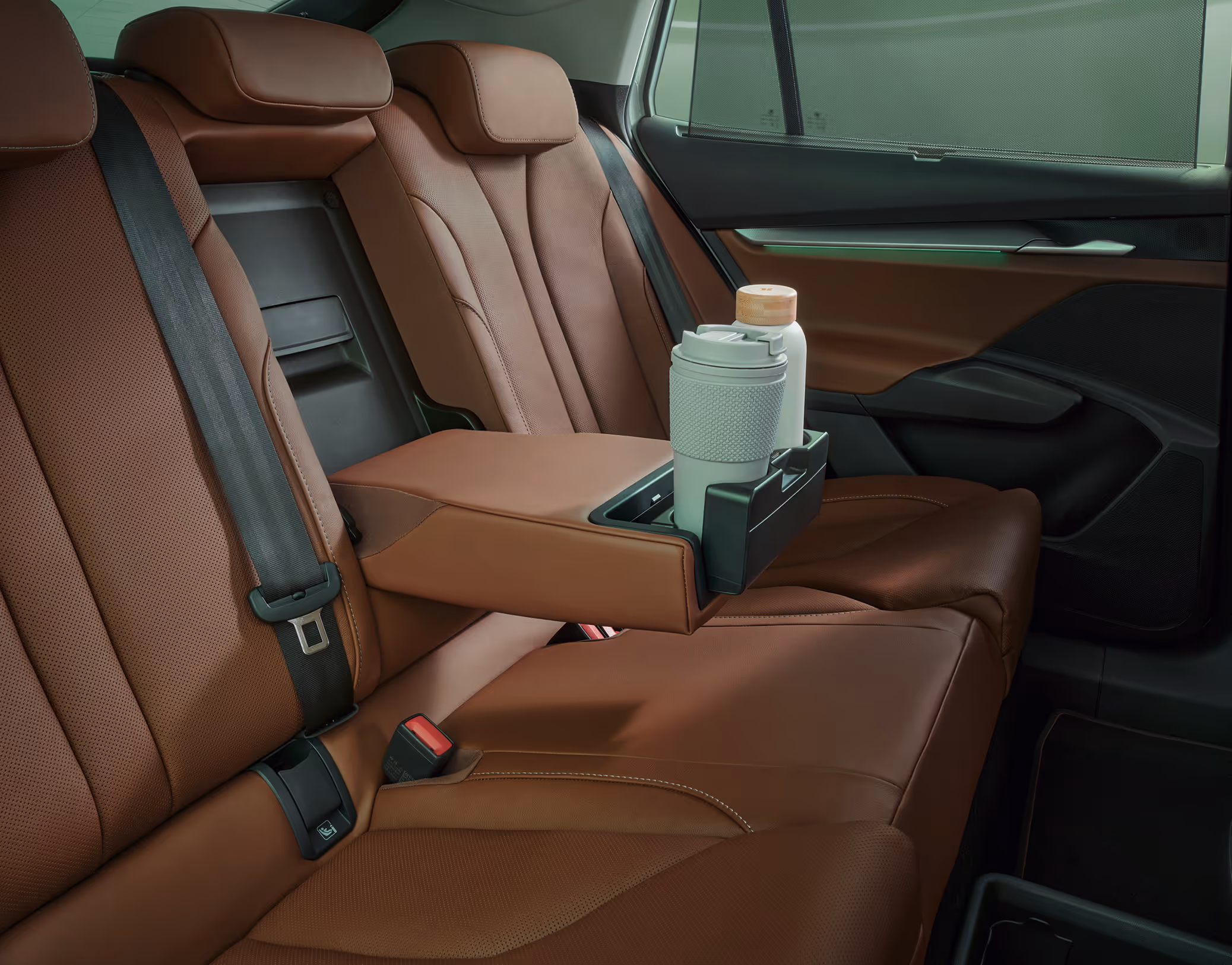 Aufnahme der Rückbank des Škoda Enyaq in der Design Selection „ecoSuite“ mit cognacbraunem Lederbezug. Die heruntergeklappte Mittelarmlehne verfügt über integrierte Getränkehalter, in denen ein Reisebecher und eine Flasche sicher abgestellt sind.