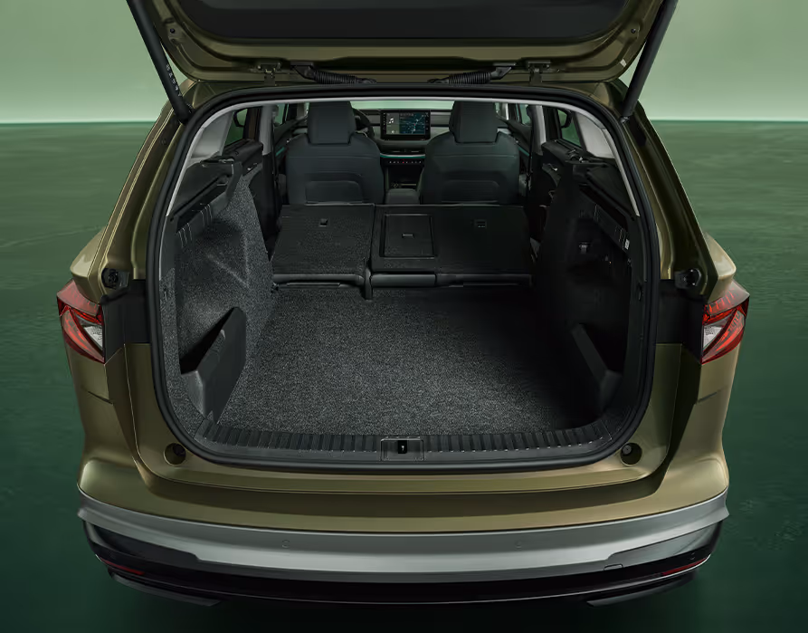 Blick in den geöffneten, leeren Kofferraum des Škoda Enyaq in der Farbe Olibo-Grün Metallic vor grünem Studiohintergrund. Das Bild zeigt das große Ladevolumen und die ebene Ladefläche.