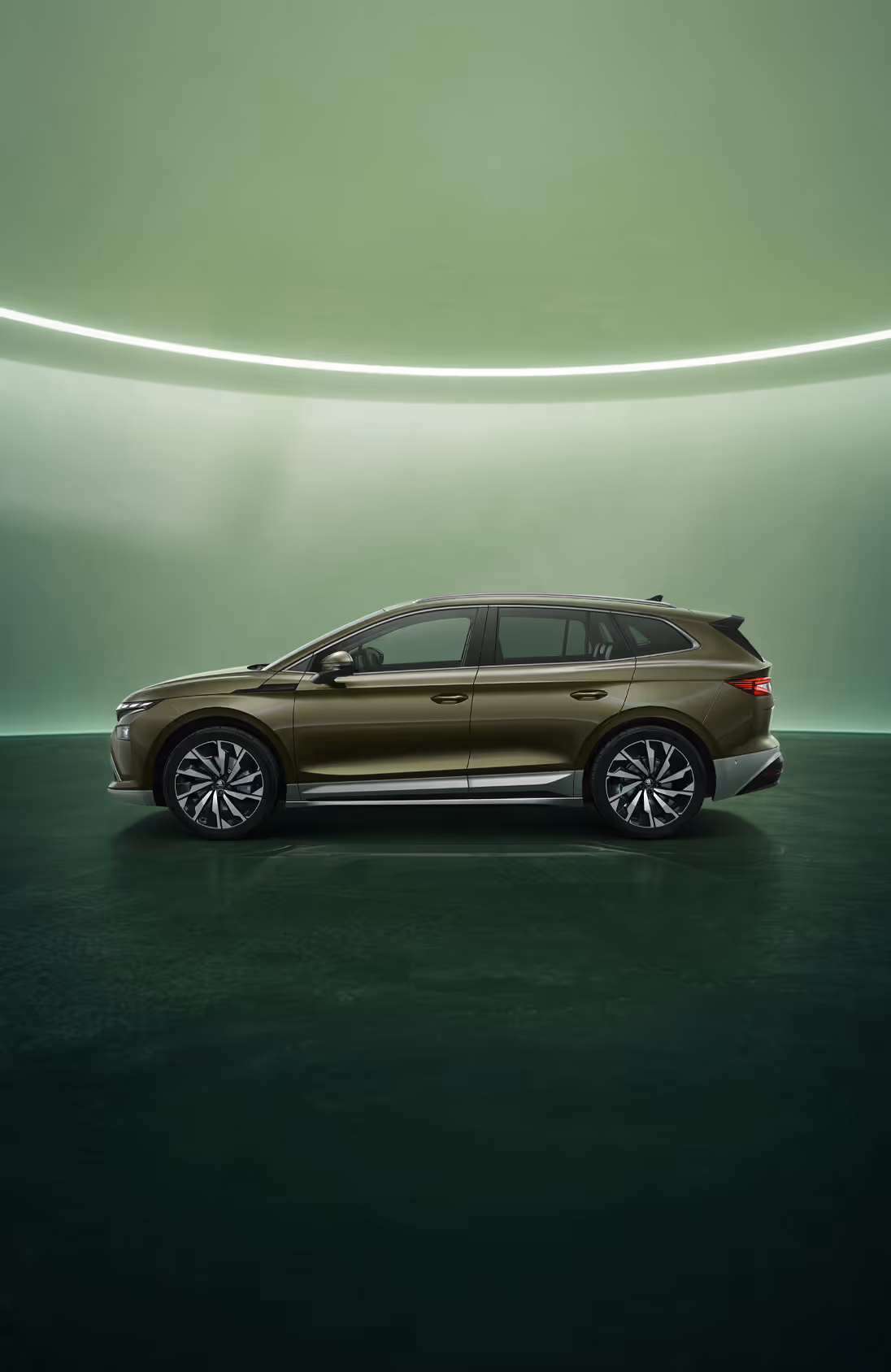 Seitenansicht des Škoda Enyaq in der Farbe Olibo-Grün Metallic vor einem grünen Studiohintergrund. Das Fahrzeug zeigt seine klare Linienführung, die robusten Radkästen und die aerodynamische Silhouette.