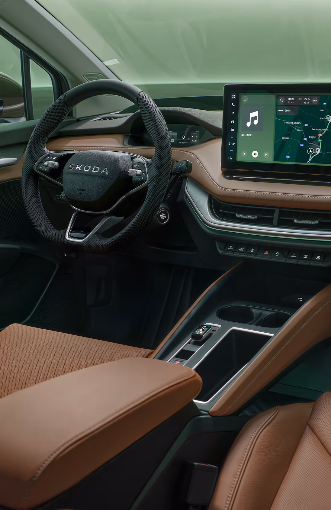 Innenansicht des Cockpits des Škoda Enyaq. Das Interieur ist mit braunem Leder und dunklen Materialien gestaltet. In der Mitte des Armaturenbretts befindet sich ein großer Infotainment-Bildschirm, der eine Navigationskarte anzeigt. Im unteren rechten Bildbereich steht auf einer dunkelgrün abgesetzten Fläche der Schriftzug „Smarte Details“.